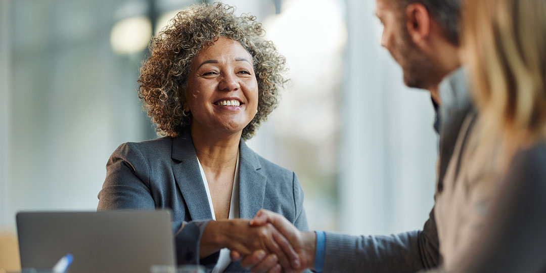 A woman sits at a laptop shaking a mans hand