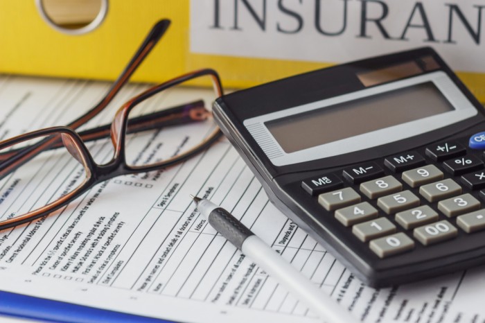 Folder labeled "Insurance", calculator, pair of glasses, and fill out form sitting on a desk