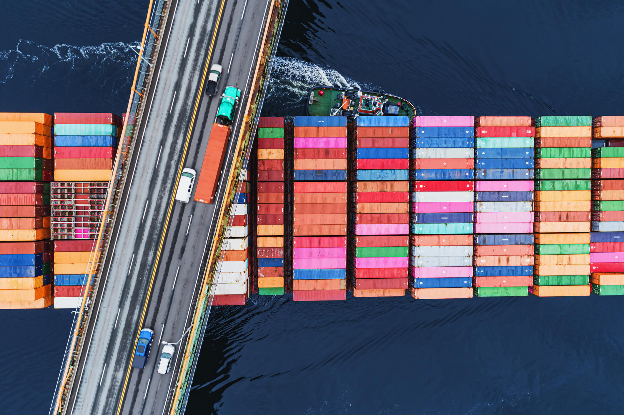 Bridge with truck and cars over a boat with freight storage boxes on the water