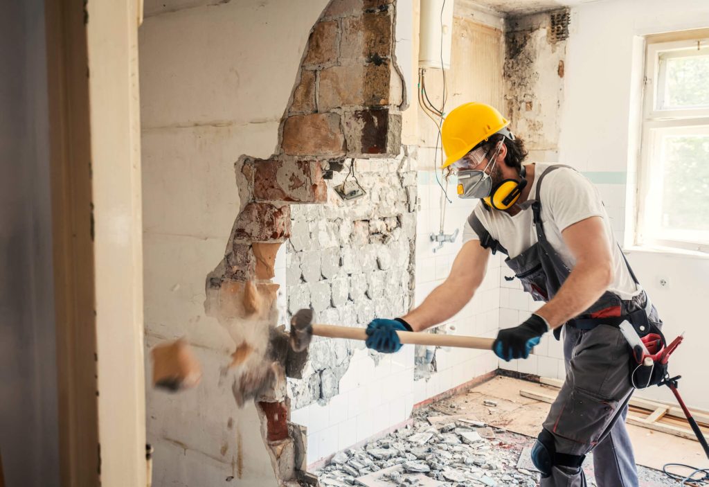 Man with construction helmet and hammer knocking down a wall