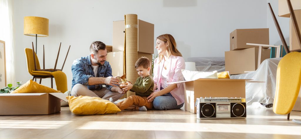 Happy family with one child starting new life in new apartment. They are unpacking boxes and talking to the child while sitting on the floor