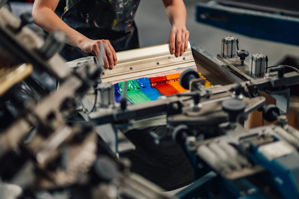 Close up of graphic worker's hands screen printing with squeegee.