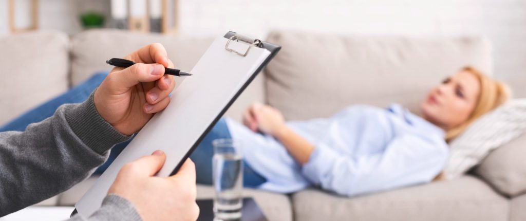 Doctor jotting down notes while patient lays on a couch