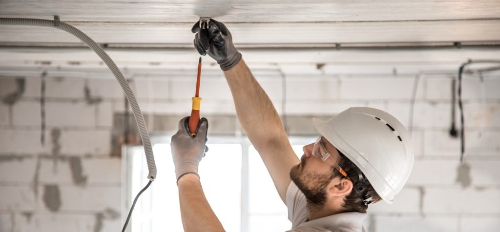 Male construction worker with safety helmet working on attaching a cord to the ceiling.